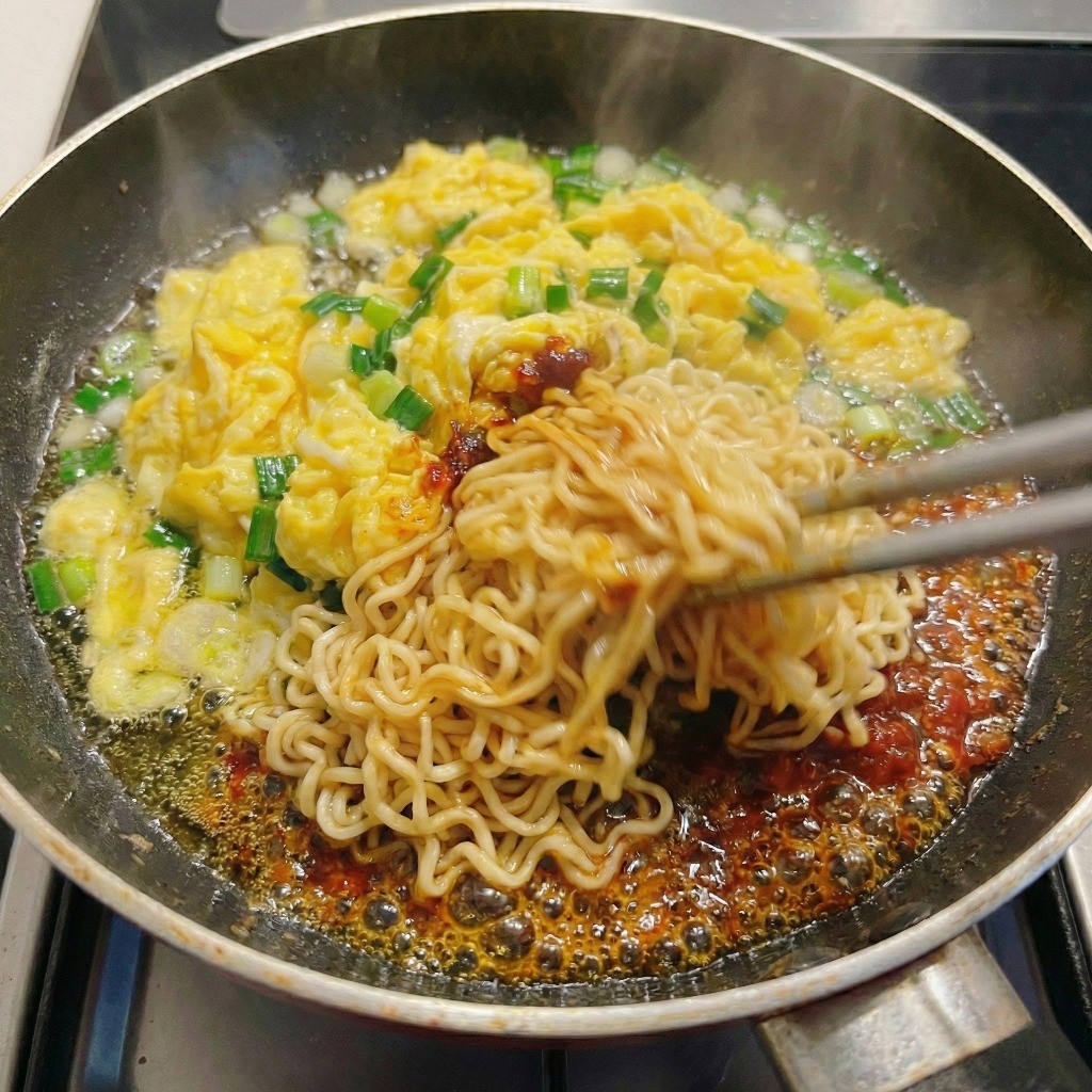 볶은 소스와 재료에 삶은 면을 넣고 센 불에 볶아 비빔면 팟타이를 완성하는 모습