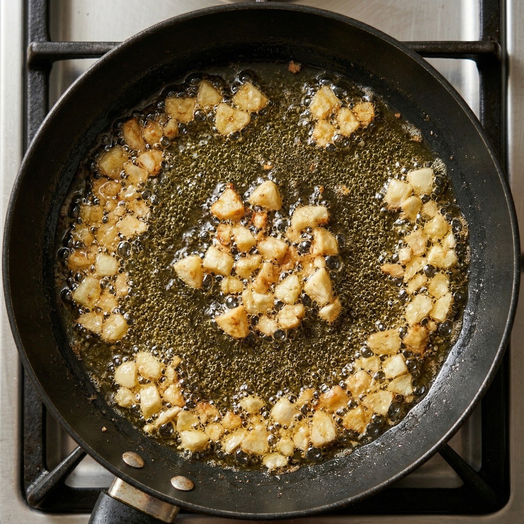 이연복 공심채 볶음 레시피 3단계: 달궈진 식용유에 거칠게 으깬 마늘을 넣어 고소한 마늘 기름을 내는 과정