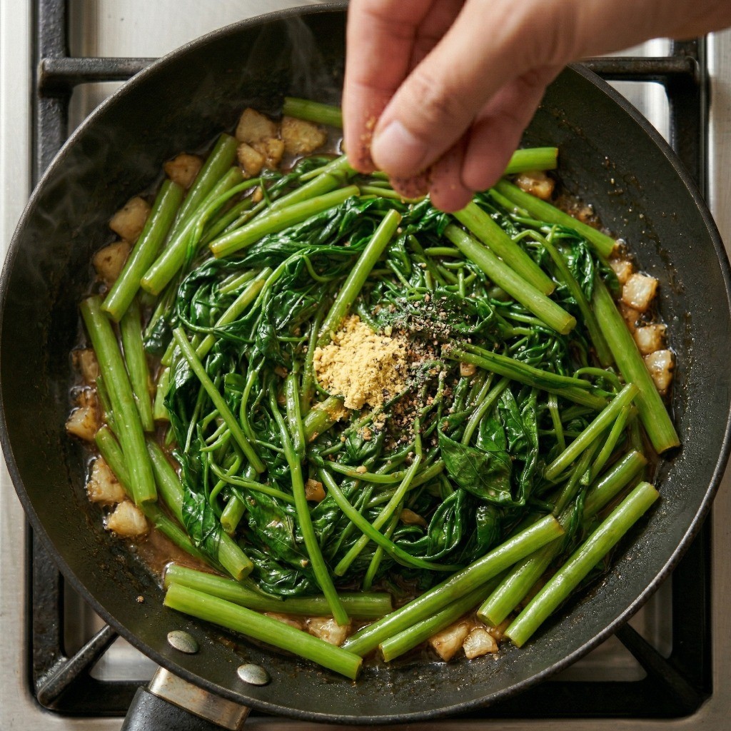 이연복 공심채 볶음 완성 6단계: 치킨스톡과 후추를 넣어 식당 모닝글로리 볶음의 깊은 감칠맛을 내며 마무리하는 모습