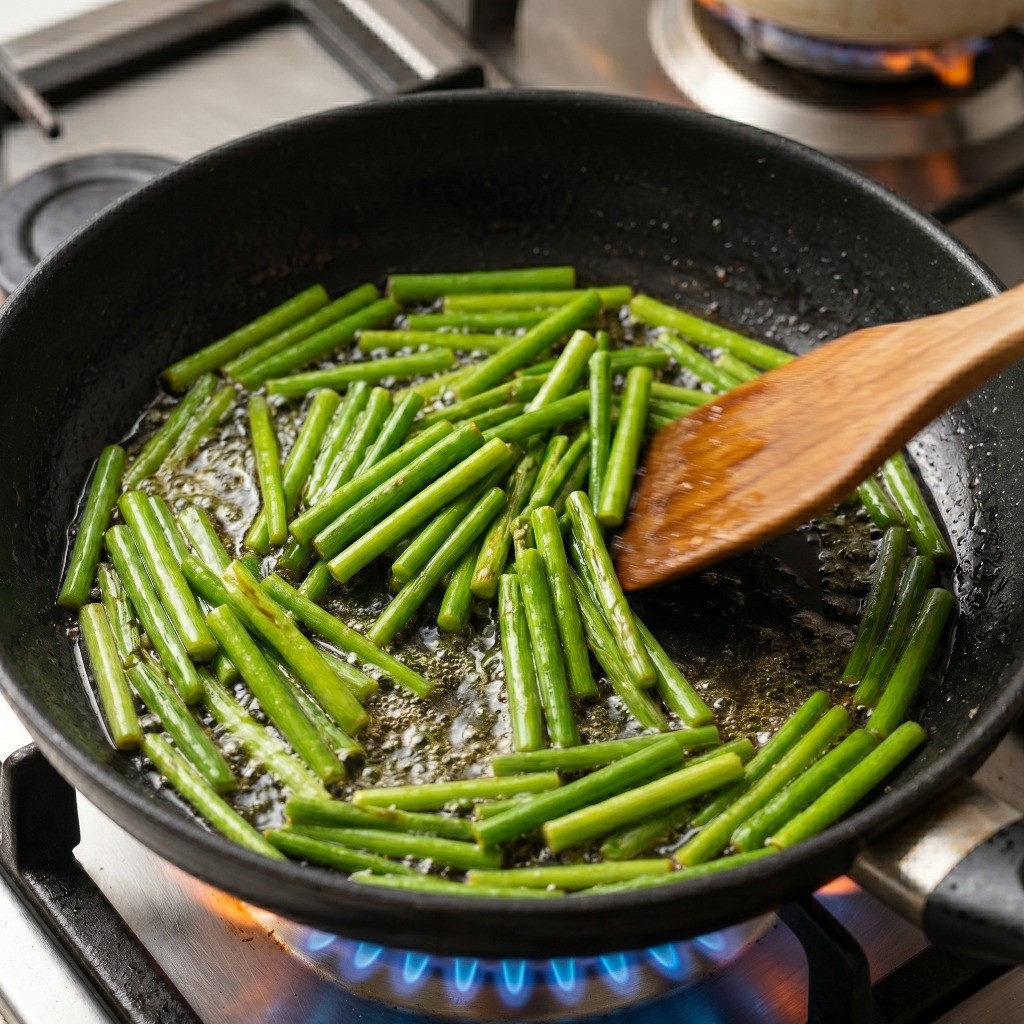 프라이팬에 식용유를 넉넉히 두르고 손질한 마늘쫑을 튀기듯이 볶아 풍미를 올리는 모습