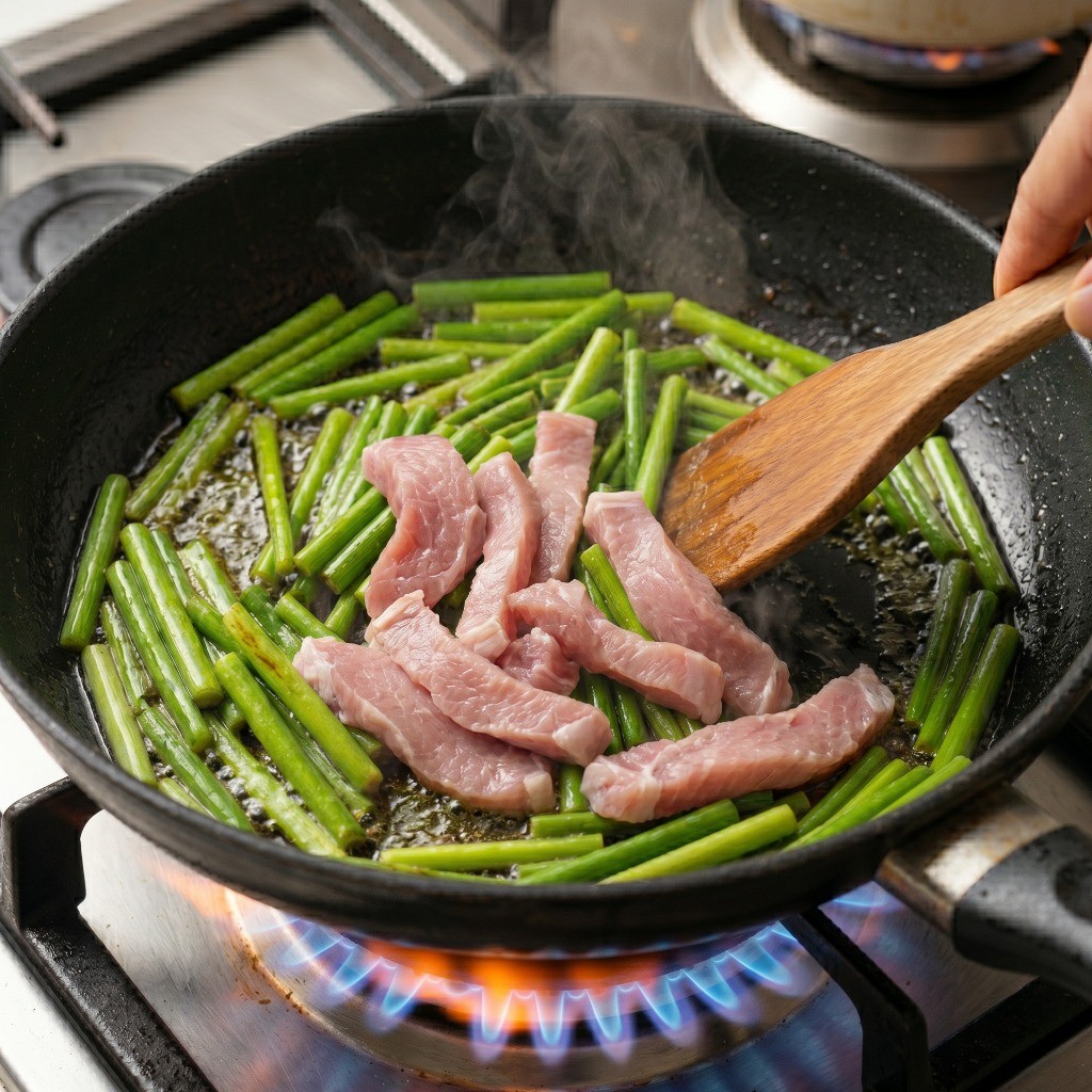 마늘쫑을 볶던 팬에 썰어둔 돼지고기를 넣고 붉은 기가 없어질 때까지 함께 볶는 모습