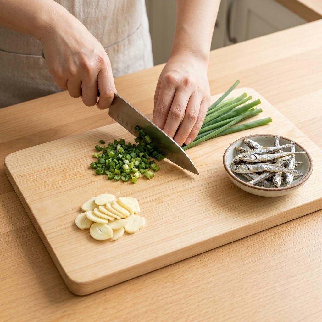 프라이드 멸치에 넣을 마늘을 편 썰고 대파를 잘게 썰어 도마 위에 준비하는 모습